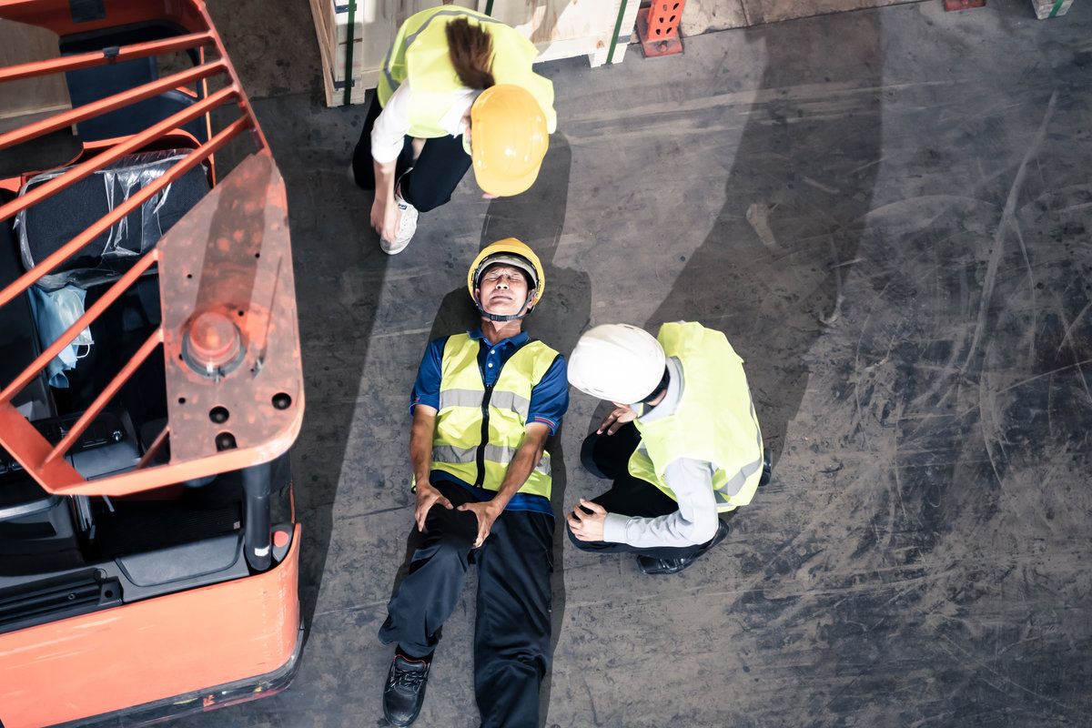 Asian old mature man worker had accident broken his leg lying near forklift truck on floor in warehouse factory. Two supervisors found and coming for help. Insurance for industrial business