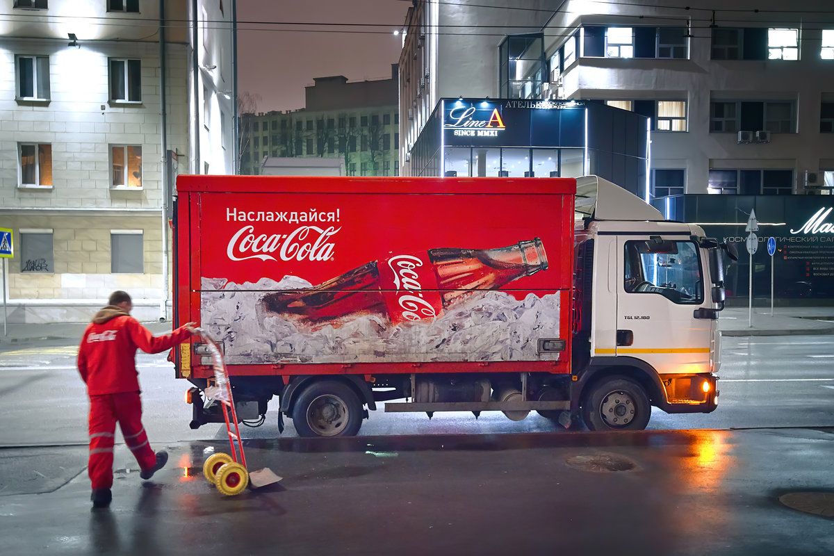 Minsk, Belarus. Jan 2020. Coca Cola delivery truck. Coca-Cola lorry delivering goods to restaurant, shop, cafe and pub. Worker with hand trolley deliver food and beverages.