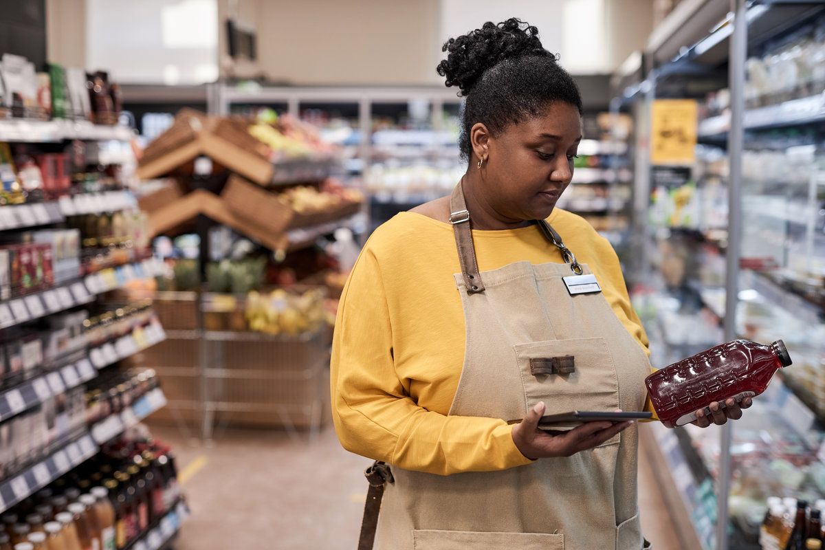 Waist up portrait of young black woman working in supermarket and doing stock inventory